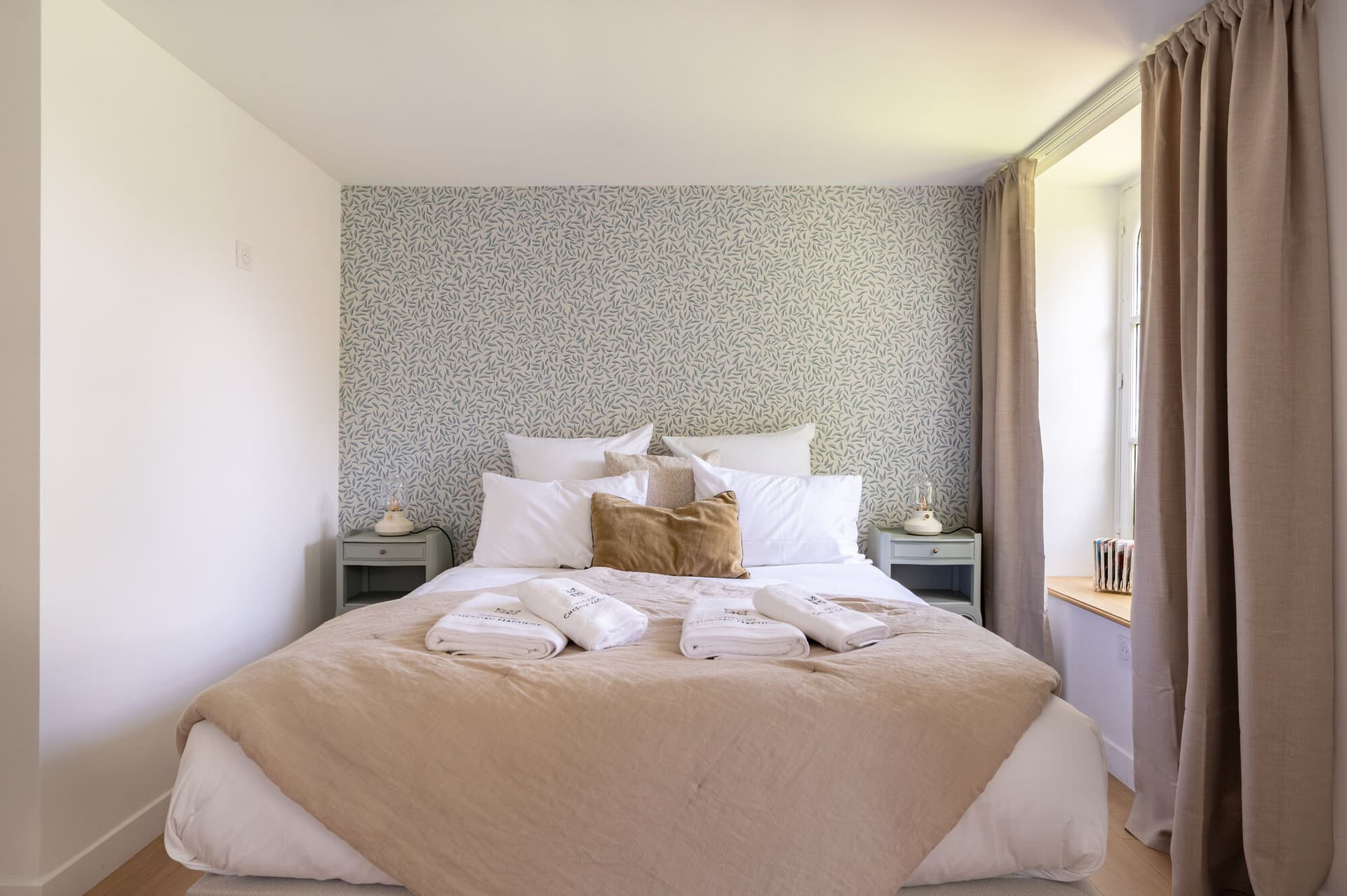 Chambre double lumineuse avec linge blanc, coussins et rideaux en lin